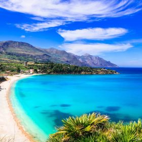 Panoramica di una splendida spiaggia in Sicilia con mare cristallino, sabbia dorata e montagne sullo sfondo.
